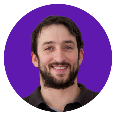 A man with dark hair and a beard is smiling at the camera, posed against a solid purple circular background.