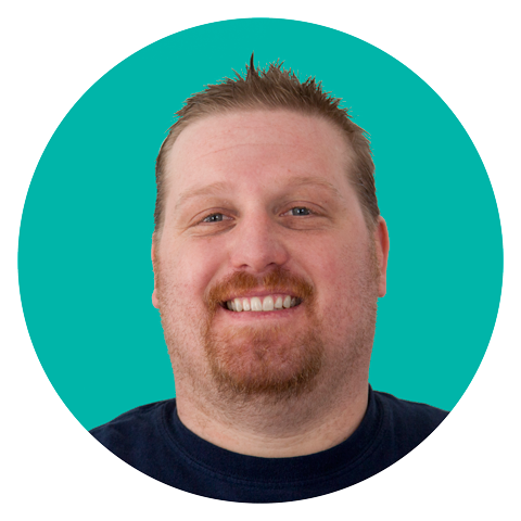 A man with short light brown hair, a beard, and a mustache is smiling at the camera. He is wearing a dark shirt and is in front of a teal circular background.