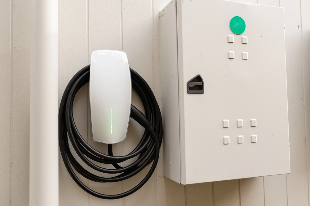 A wall-mounted electric vehicle charging station, expertly installed by an electrician, features a coiled cable next to a white electrical control box.