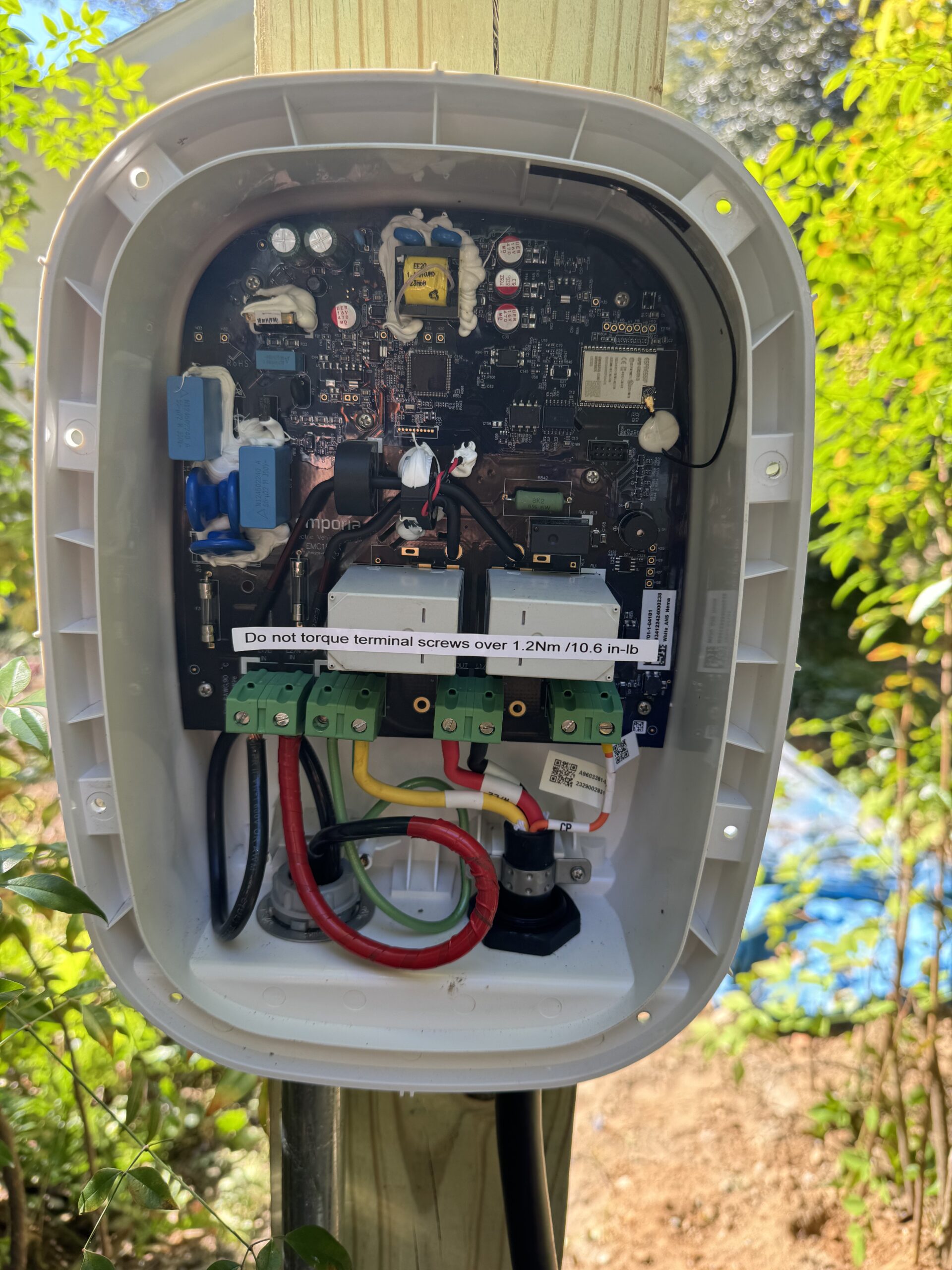 An open electrical control box mounted on a wooden post, showing exposed wiring, circuit board, and terminal connections.